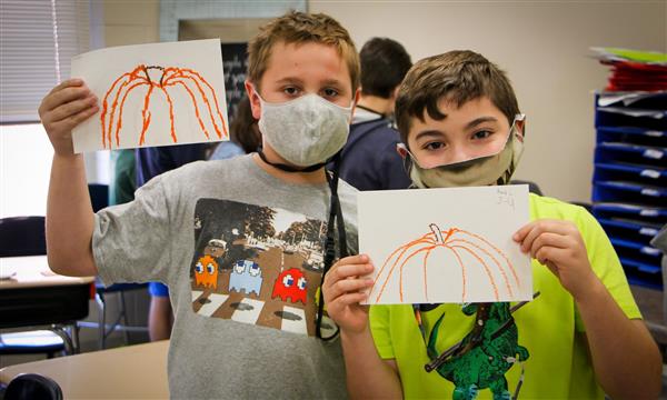 Two boys hold up pumpkin drawings